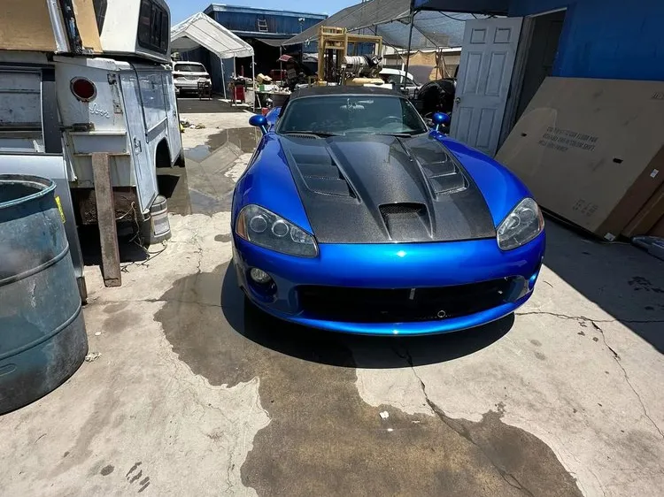 Blue sports car with a carbon fiber hood parked in the shop yard after body work