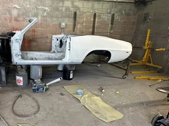 Stripped classic convertible body shell in white primer on a stand inside the shop