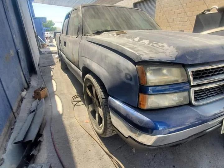 Blue pickup truck with primer patches on the hood and fender during body work