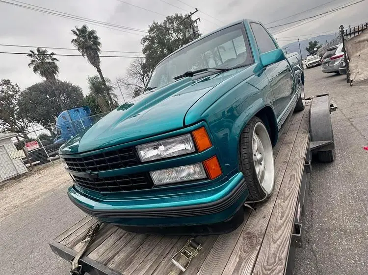 Teal Chevrolet pickup with fresh paint strapped to a trailer for delivery